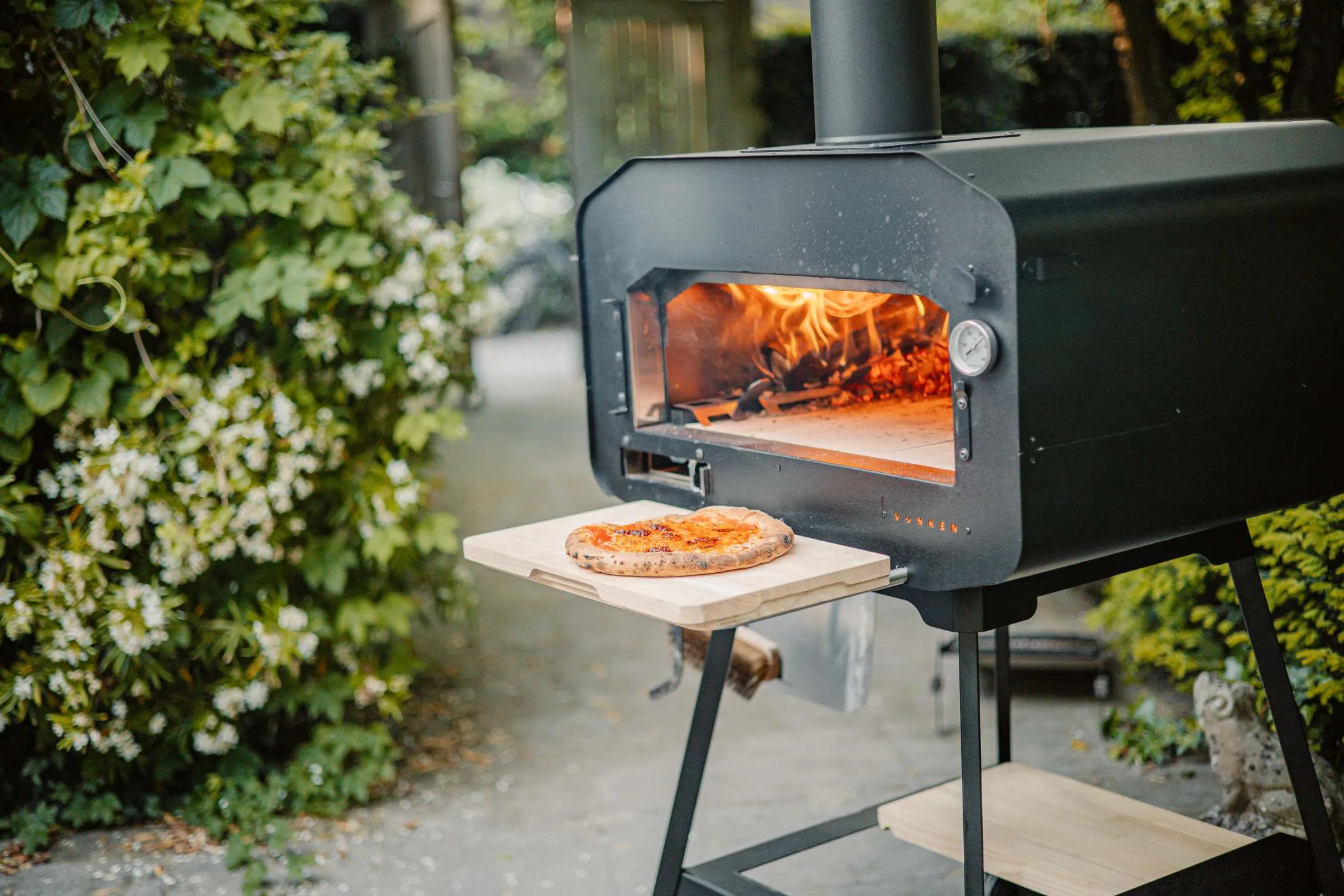 Man die een pizza in een houtgestookte oven schuift, genietend van buiten koken